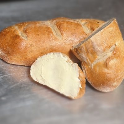 A piece of buttered French bread and a heel of bread leaning against a full French loaf.