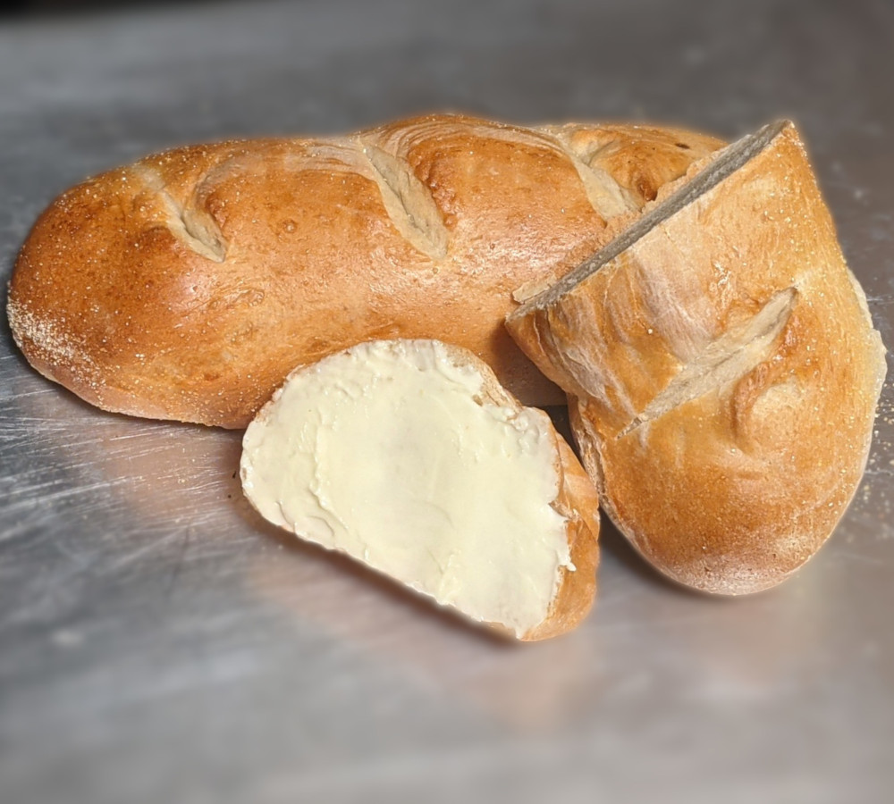 A piece of buttered French bread and a heel of bread leaning against a full French loaf.