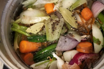 An over head shot of the chicken stock cooking with all the vegetables floating on top.