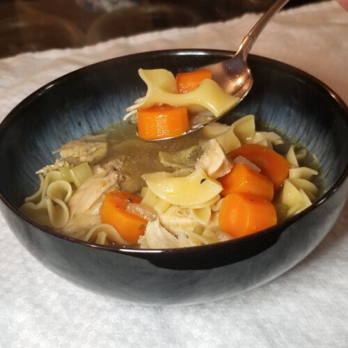 A bowl of comforting chicken noodle soup with a spoon being lifted to eat.