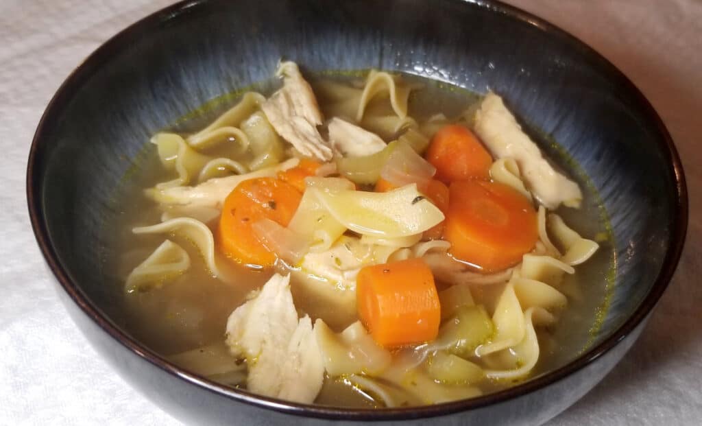 A close up of chicken noodle soup in a bowl.