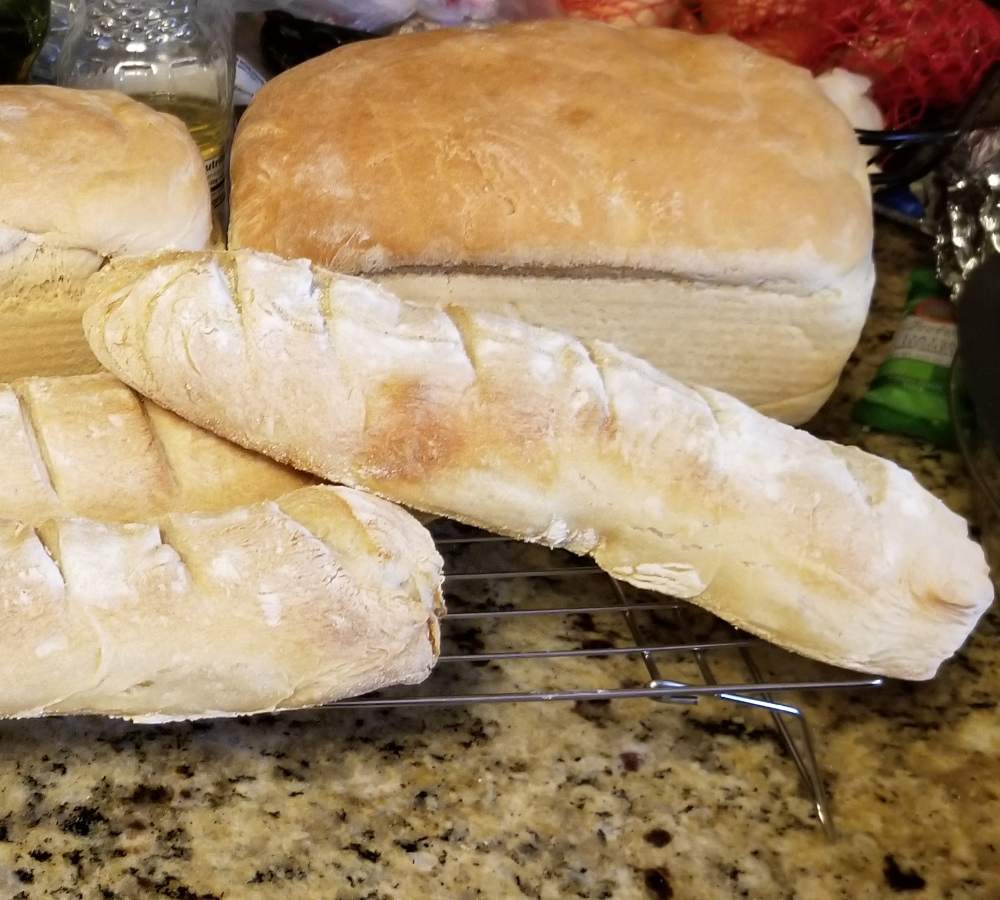 A stack of homemade breads including sourdough, french bread, and white bread