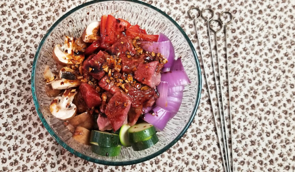 Beef, mushrooms, zucchini, pepper, and red onion in a bowl covered with kabob marinade.