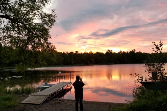 My husband standing at the edge of a lake as the sun sets