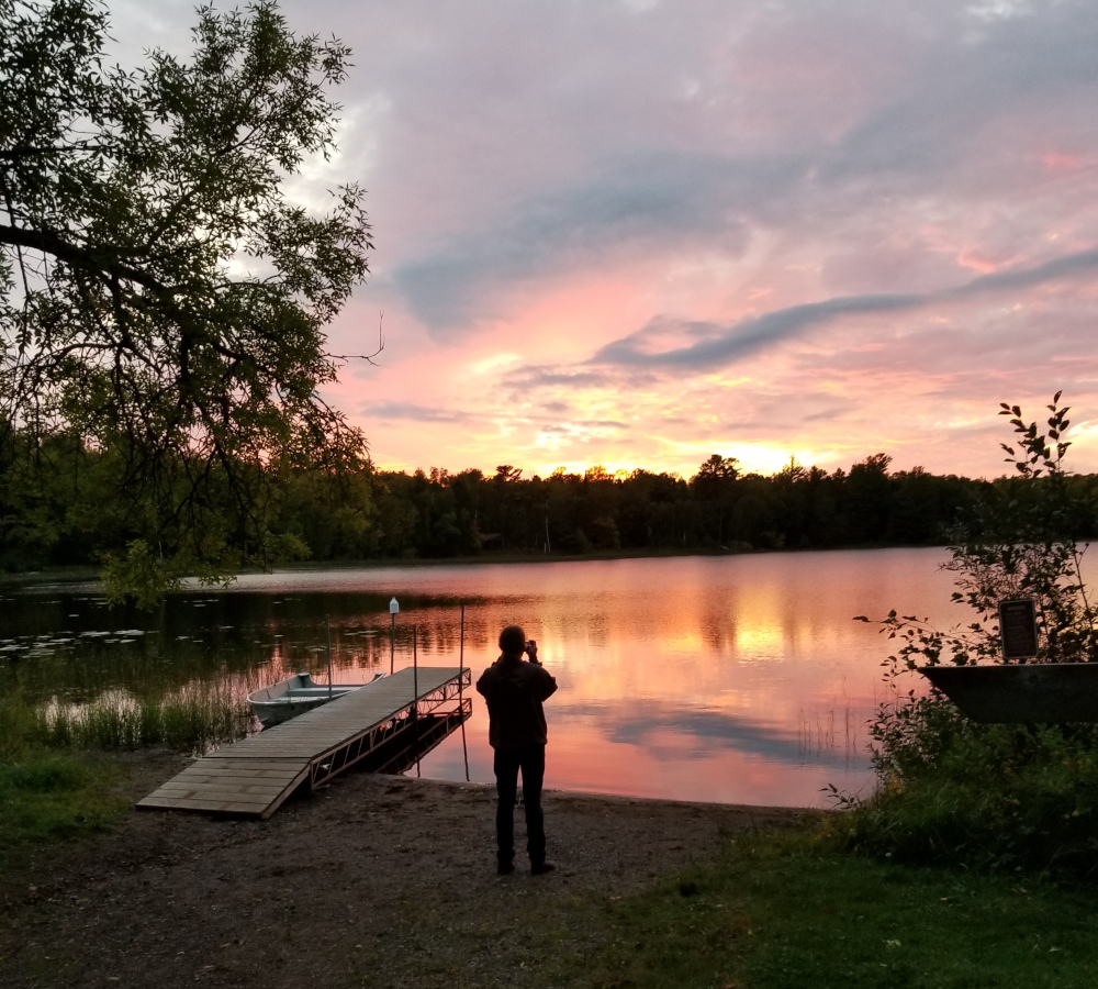 My husband standing at the edge of a lake as the sun sets