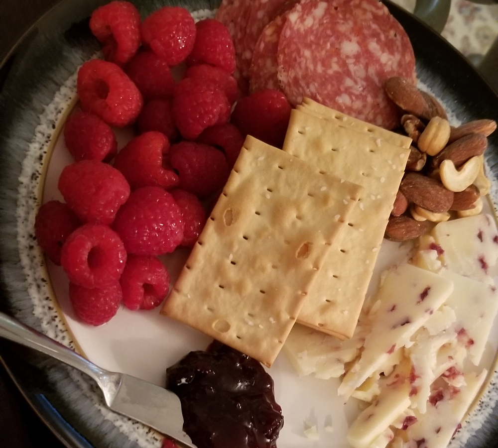 a charcuterie plate with raspberries, salami, crackers, cheese, mixed nuts, and jam