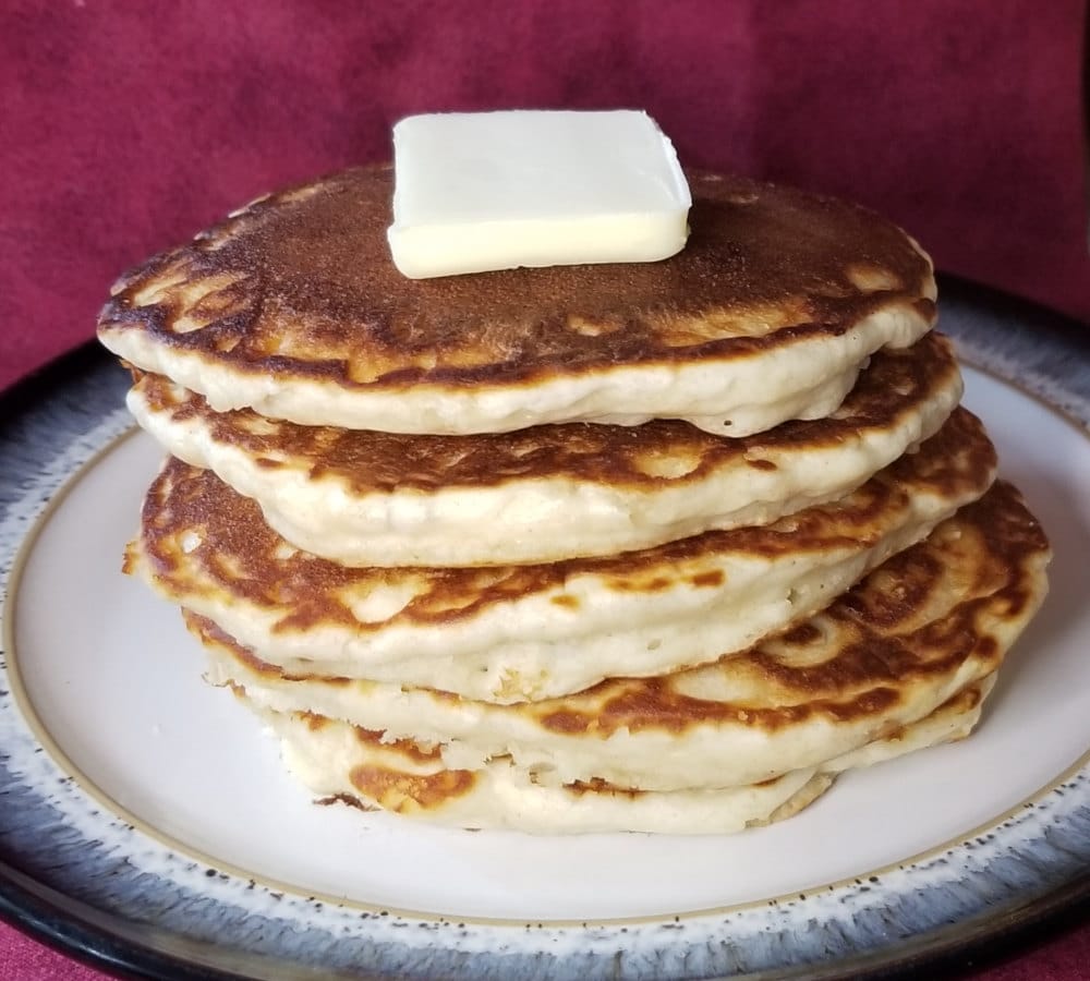 Stacked pancakes on a plate, topped with a pat of butter. 