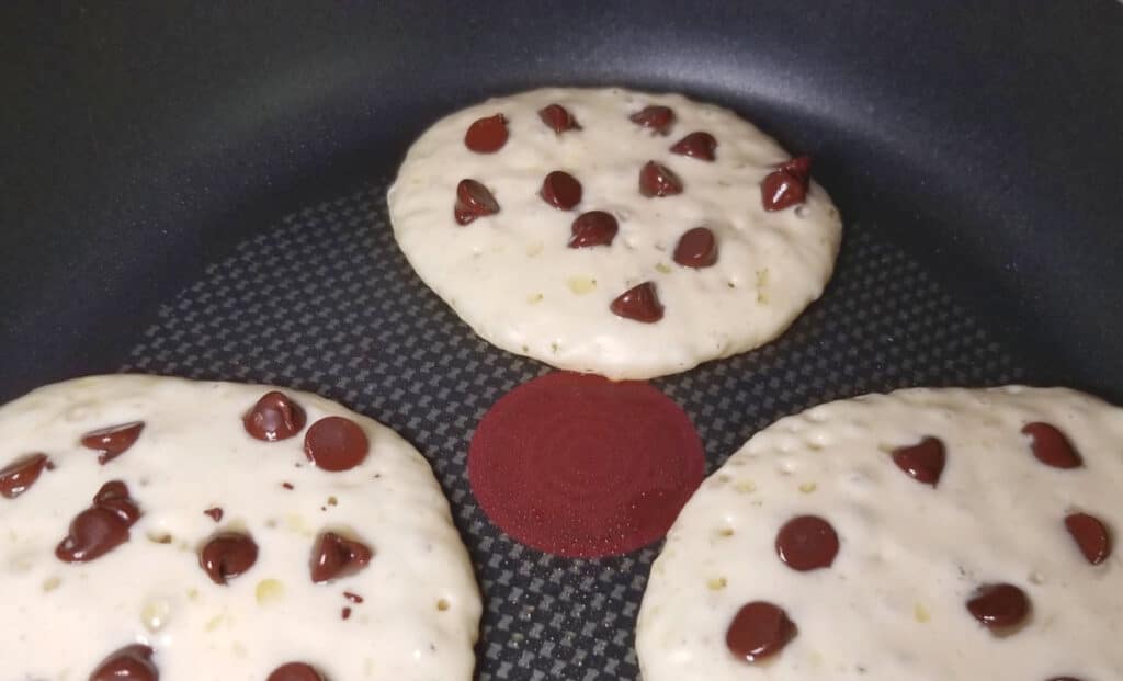 Chocolate chip pancakes cooking in a pan. 