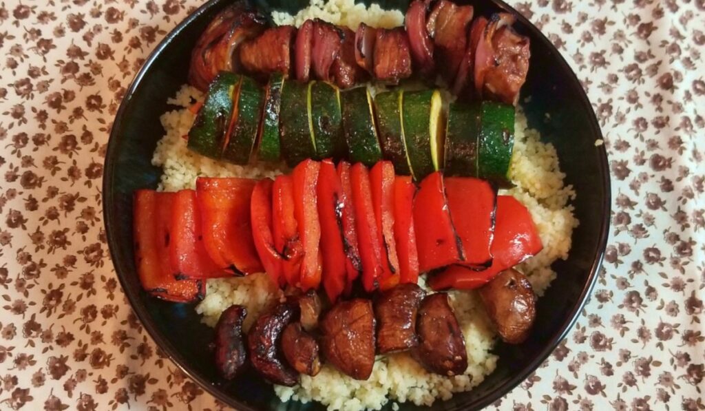 Skewers of grilled vegetable and steak kabobs served over couscous