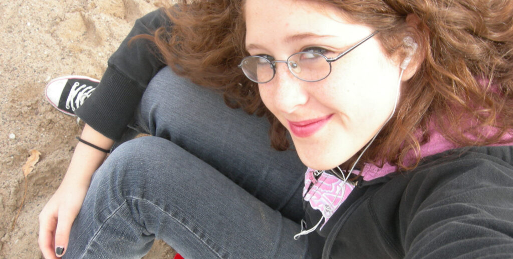 A teenage picture of myself sitting on the beach, wearing a pair of converse shoes and with black nail polish and eyeliner.