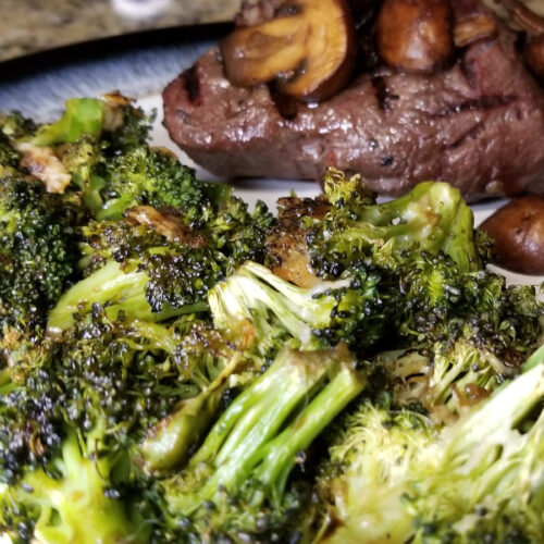 A close up of balsamic broccoli with steak and mushrooms in the background.