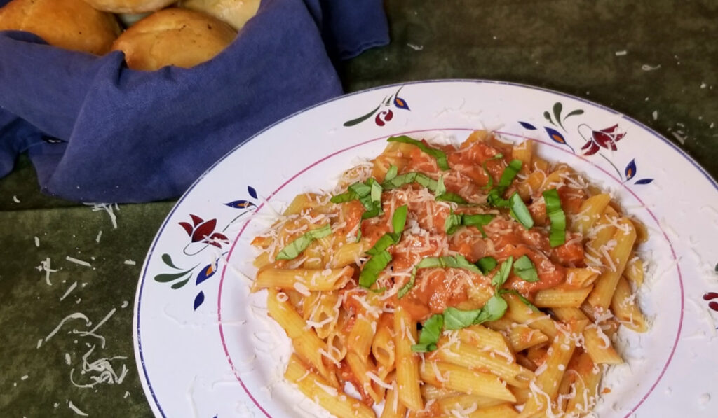 Pasta with creamy tomato sauce and a bowl of rolls.