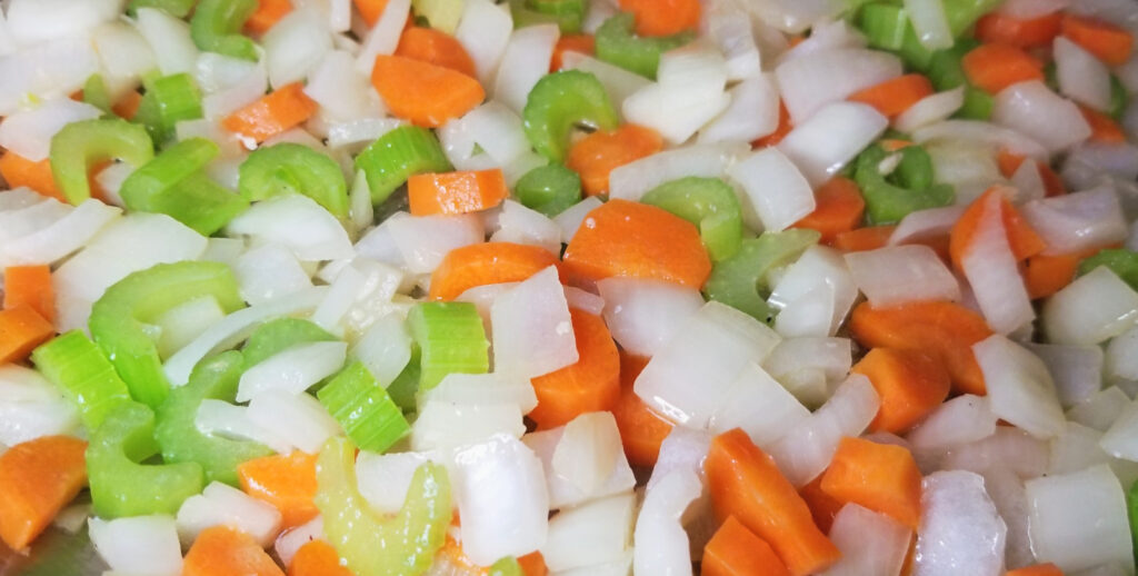 Onion, celery, and carrots, glistening with butter and sizzling in a pan. 