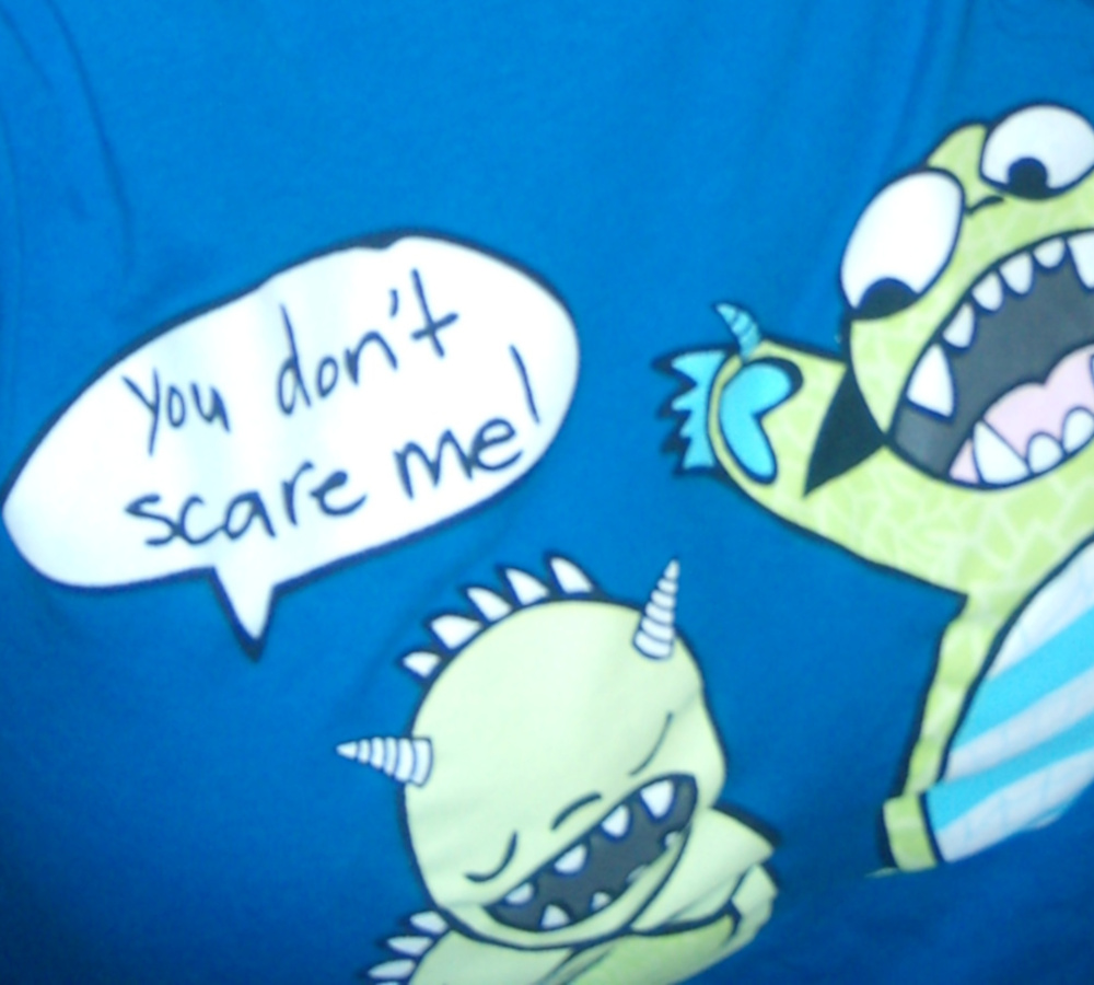 A blue shirt with pictures of two monsters. One says to the other "you don't scare me"