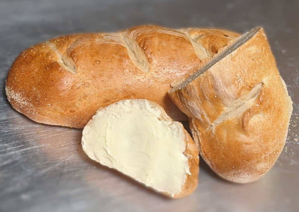 A buttered piece of french bread and a bread heel leaning against a full french loaf.