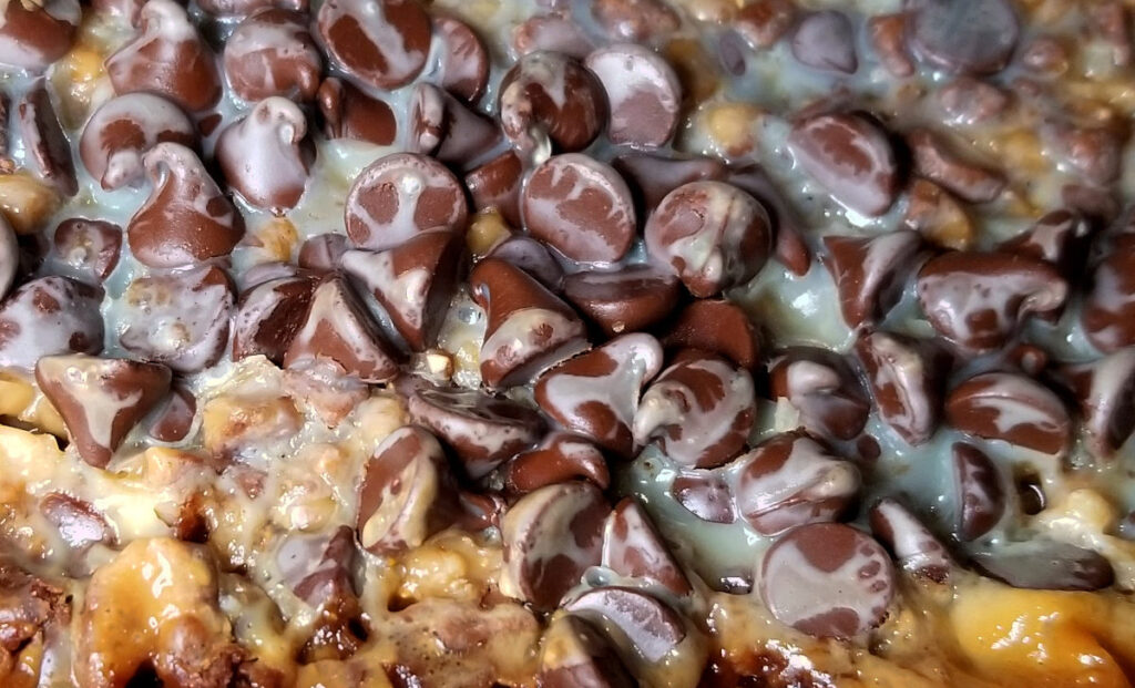 A zoomed in picture of the dark chocolate toffee bars, still in the baking pan. You can see the condensed milk caramelizing and coating the chocolate chips. 