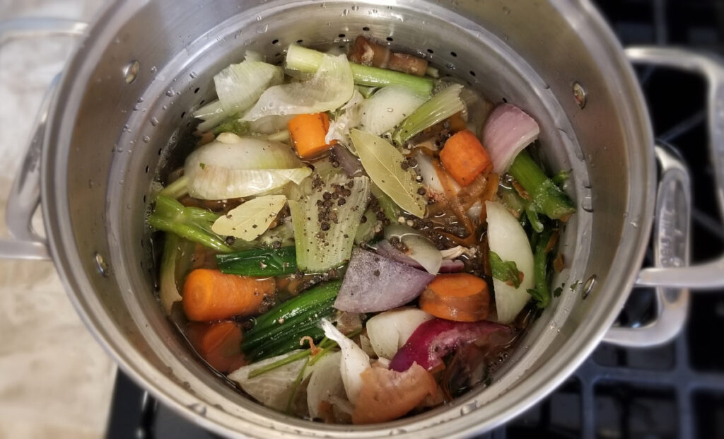 An over head shot of the chicken stock cooking with all the vegetables floating on top. 