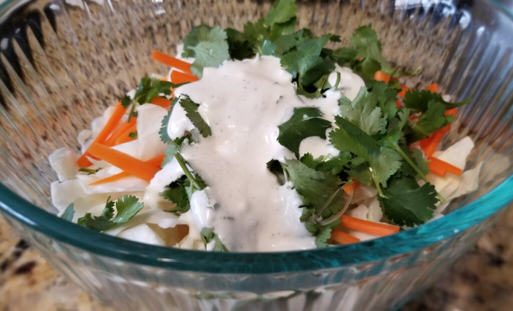 Cilantro, carrot, and cabbage with cilantro lime slaw dressing not yet fully mixed in. 