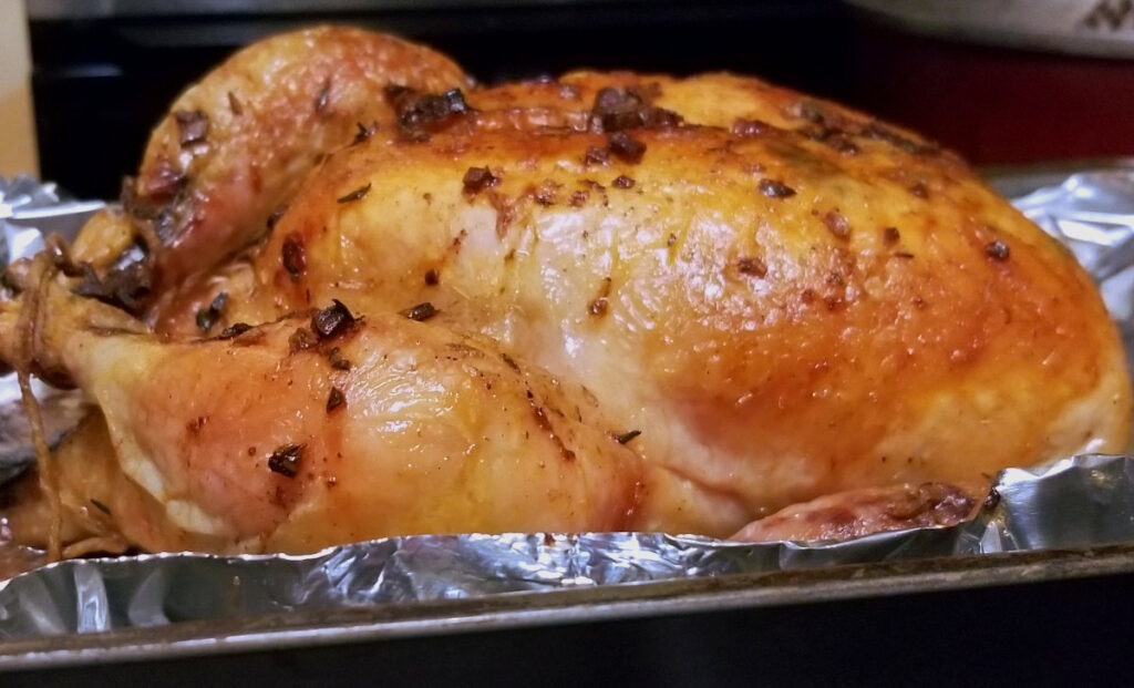 A cooked garlic butter whole chicken sitting in a baking dish with aluminum foil.