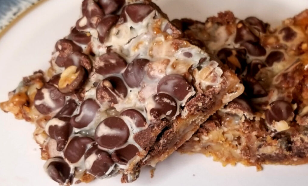 A zoomed in shot of one dark chocolate toffee bar laying on top of another on a white plate with blue and gold edges.