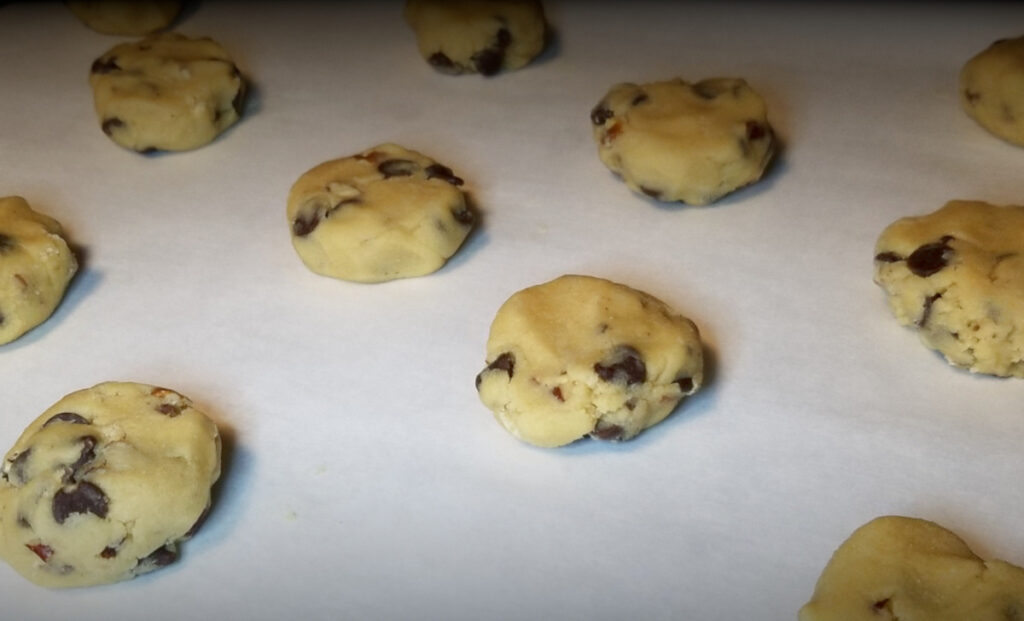 Chocolate chip cookie dough uncooked on a baking sheet with parchment paper.