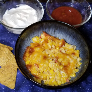 Cheesy corn dip served alongside sour cream, salsa, and tortilla chips.