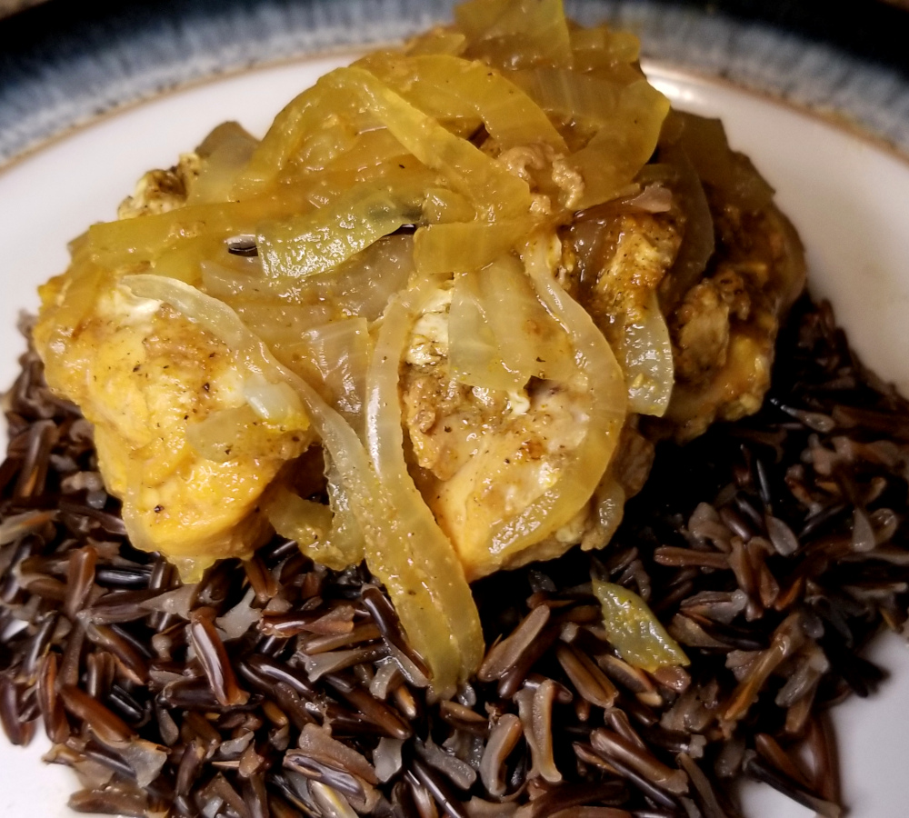 A close up of honey curry chicken on a pile of cooked wild rice.