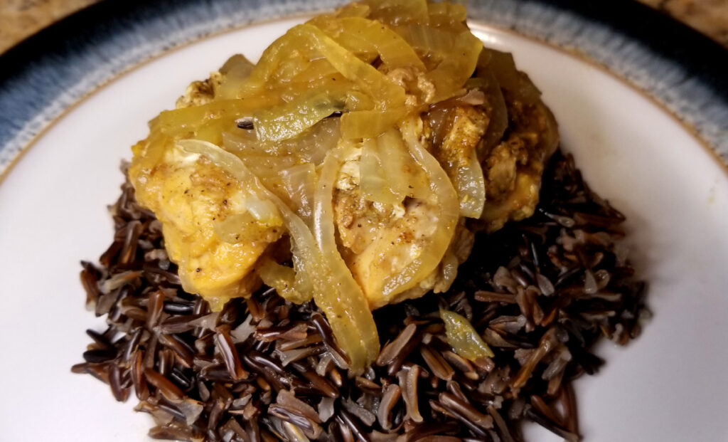 onions and honey chicken curry served on top of a pile of wild rice. 
