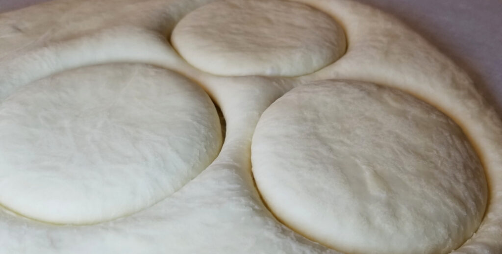 English muffin dough with flattened and cut into circles but not yet separated.