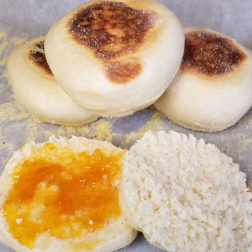 stacked english muffins in the background and an open muffin in the front with apricot jam