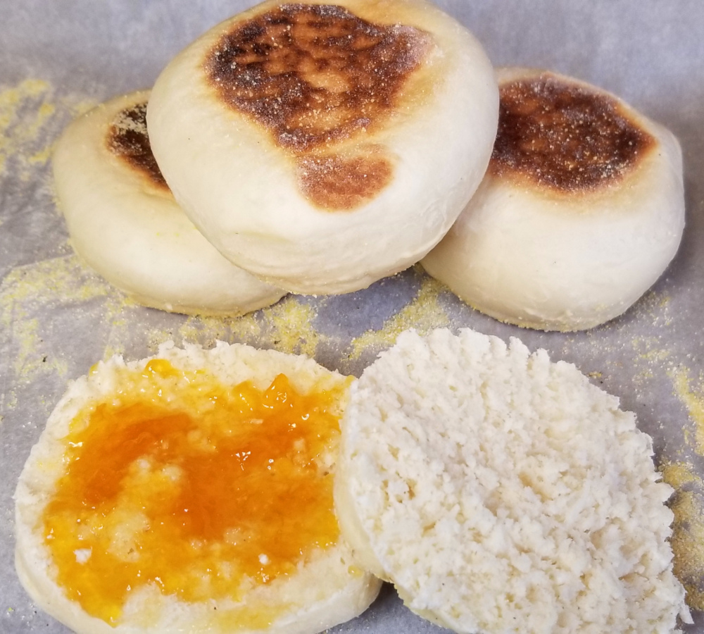 stacked english muffins in the background and an open muffin in the front with apricot jam