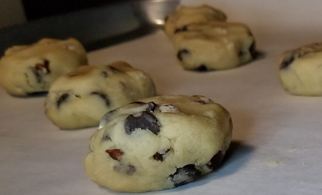 A close up of the uncooked chocolate chip cookie dough balls on a baking sheet with parchment paper. 
