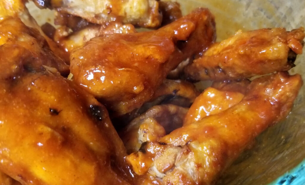 A close up of hot honey bourbon coated chicken wings in a glass bowl. 