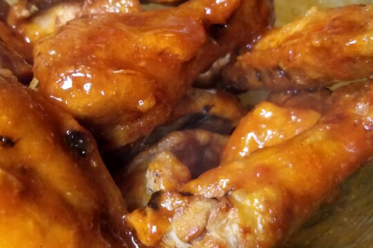 A close up of hot honey bourbon coated chicken wings in a glass bowl.