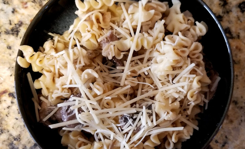 A close up of a bowl of balsamic mushroom pasta topped with shredded parmesan.