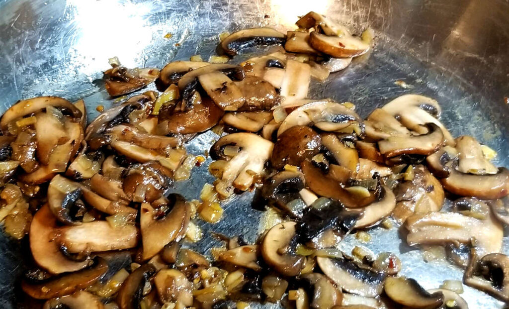 Browned mushrooms being sautéed with onions in a large pan. 