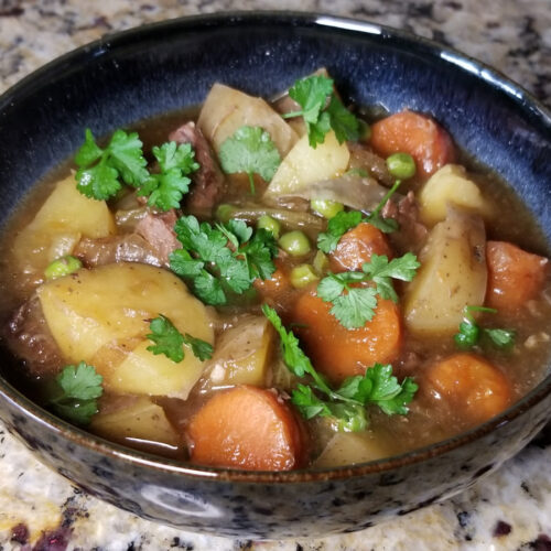 The finished beef stew served in a blue-black bowl and sprinkled with some parsley