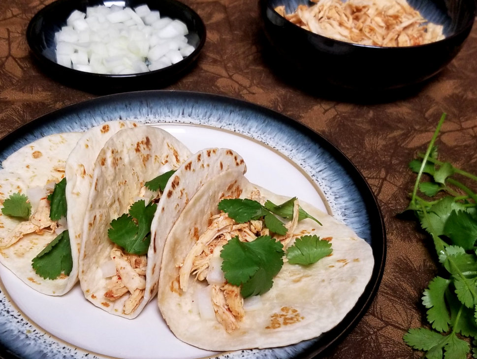 Shredded chicken tacos with cilantro and onion, with extra of all ingredients in the background.