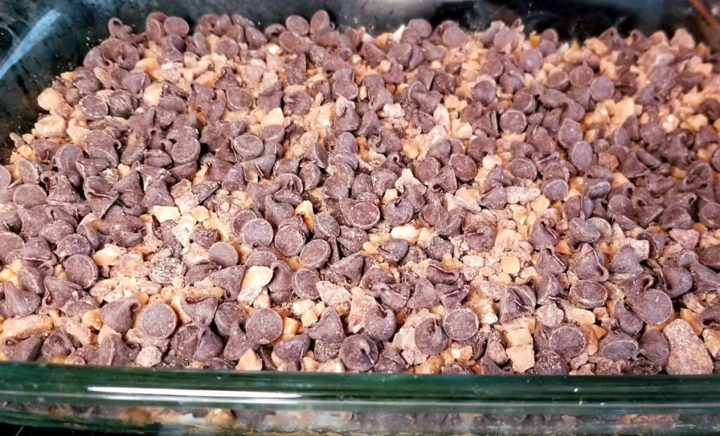 The uncooked dark chocolate toffee bar ingredients are shown layered in a glass baking dish.