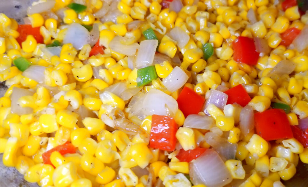 Cheesy corn dip vegetables mixed together. Yellow, red, green, and white vegetables contrast each other. 