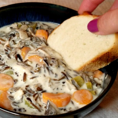 Minnesota wild rice soup being dipped into by French bread.