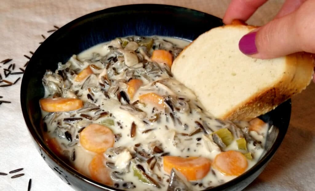 French bread being dipped in a bowl of wild rice soup.