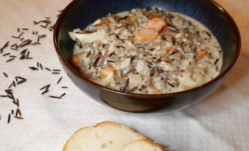 creamy wild rice soup with bread and wild rice sprinkled around. 