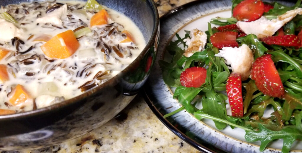 A bowl of wild rice soup alongside a plate of strawberry chicken salad