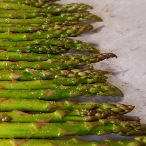 A close up of uncooked but seasoned asparagus on parchment paper.