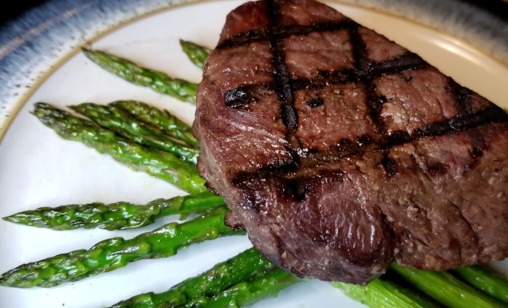 A steak with grill marks laying on top of roasted asparagus.