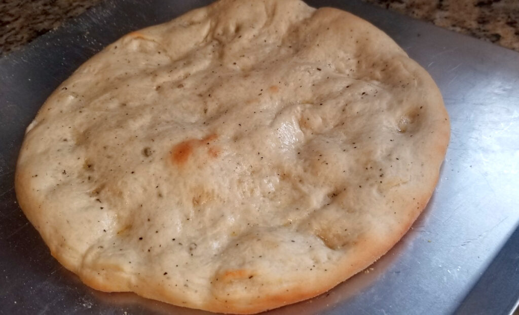 Garlic and herb pizza dough par baked and sitting on a cookie sheet.