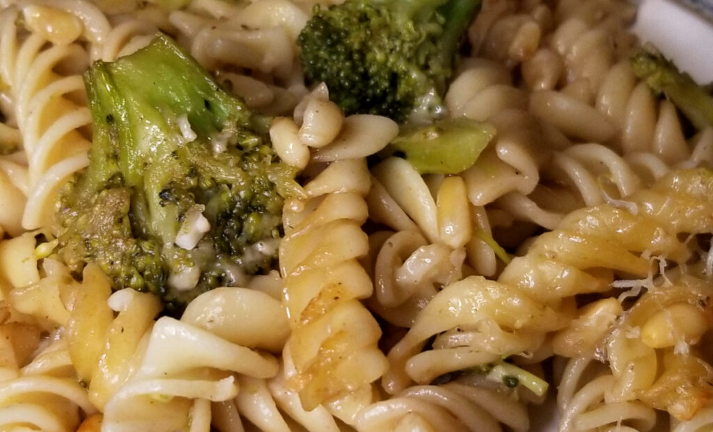 A close up broccoli pine nut pasta on a white plate. 