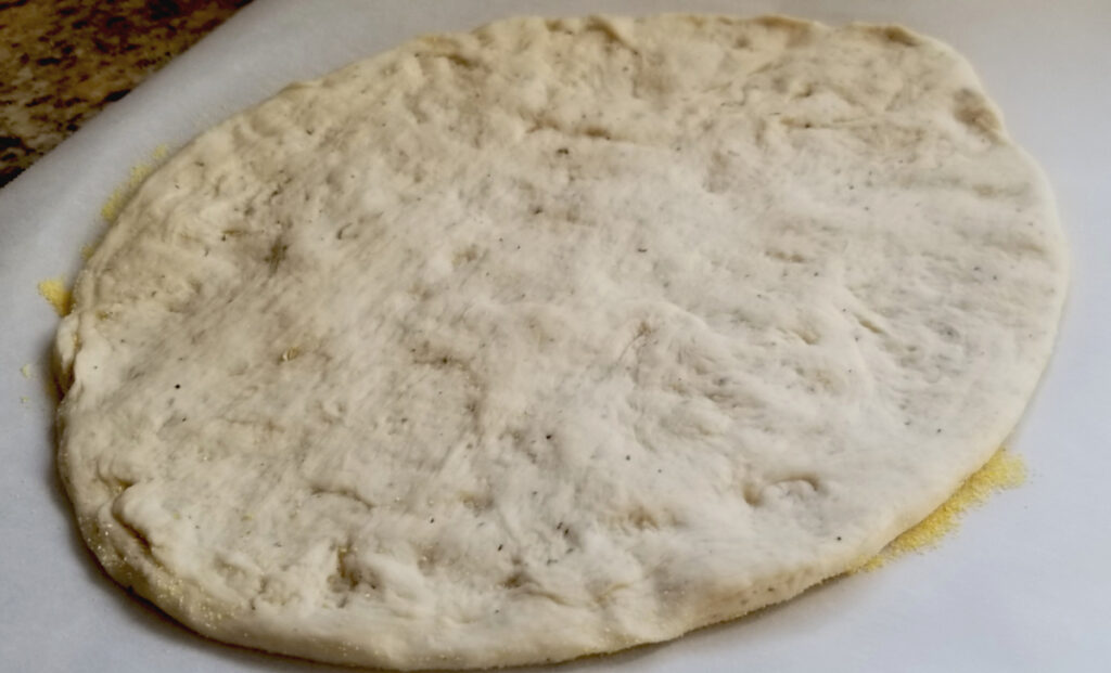 Raw garlic and herb pizza dough on parchment paper with cornmeal