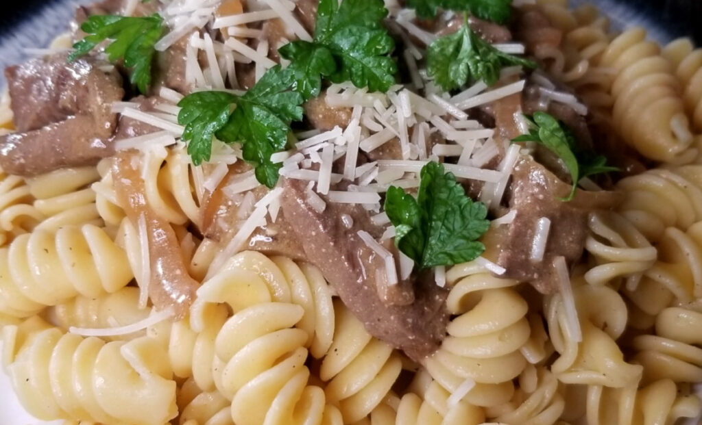 A close up of beef stroganoff on a plate sprinkled with parmesan cheese and parsley.